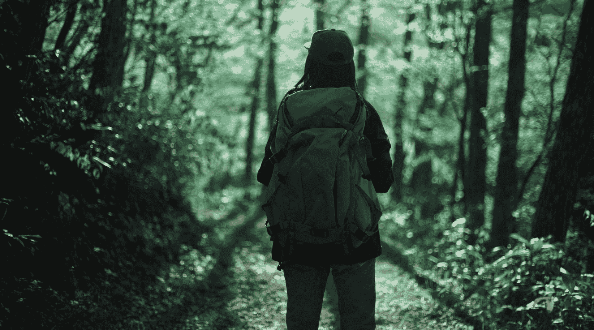 Nainen seisoo reppu selässä keskellä metsää ja katsoo eteenpäin.