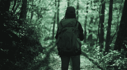 Nainen seisoo reppu selässä keskellä metsää ja katsoo eteenpäin.